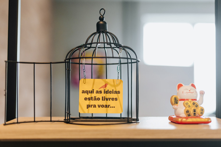 Uma gaiola aberta e um papel dentro dela, onde se lê: aqui as ideias estão livres pra voar.